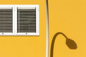 A minimalist scene featuring a yellow wall with a white window and the shadow of a lamp.