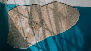 Detailed view of a wall with peeling blue paint and exposed plaster, showing textures and shadows.