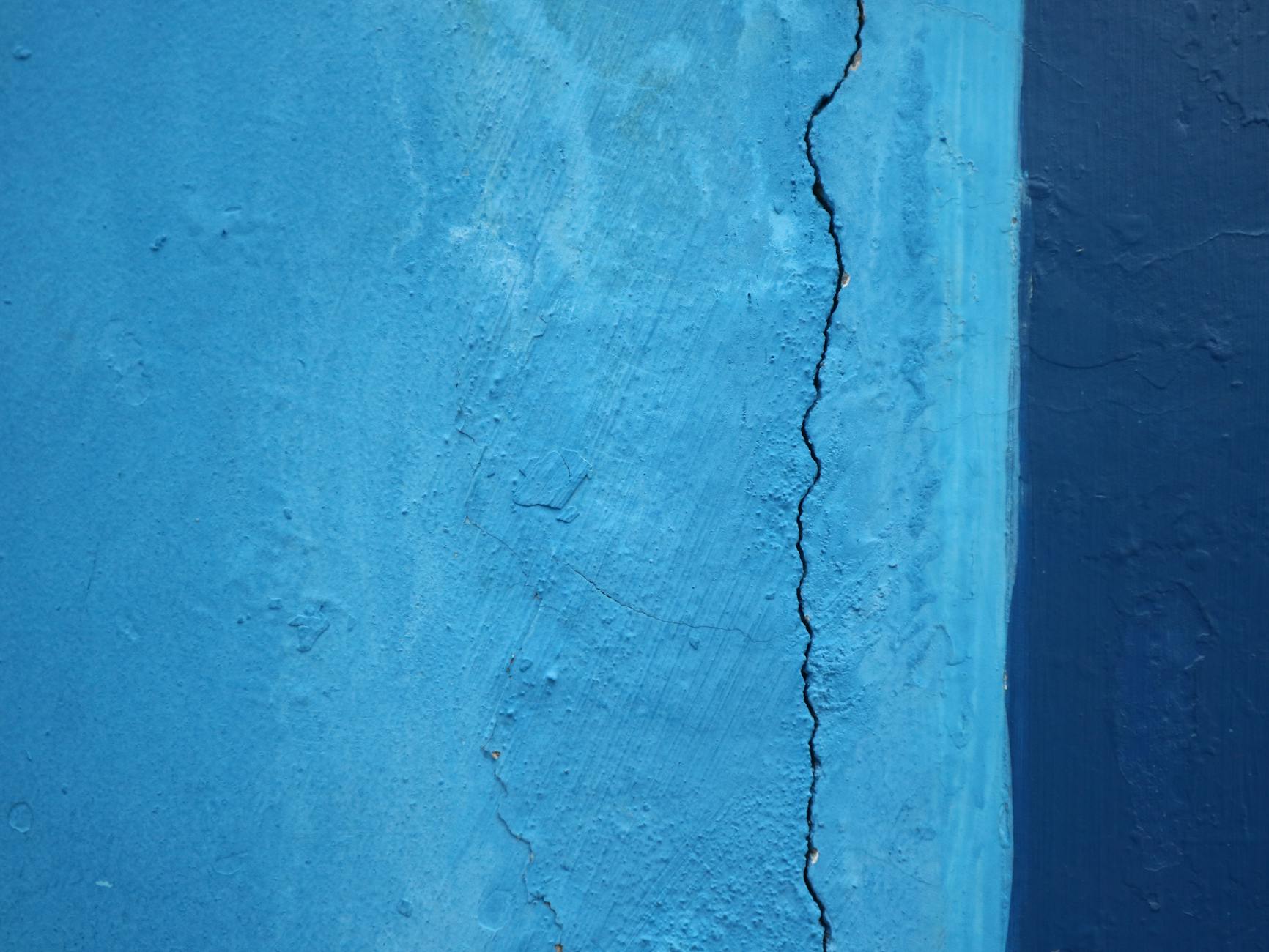 Detailed close-up of a cracked blue wall texture, revealing surface imperfections.