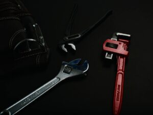 Close-up of various hand tools including wrenches and pliers on a dark surface.