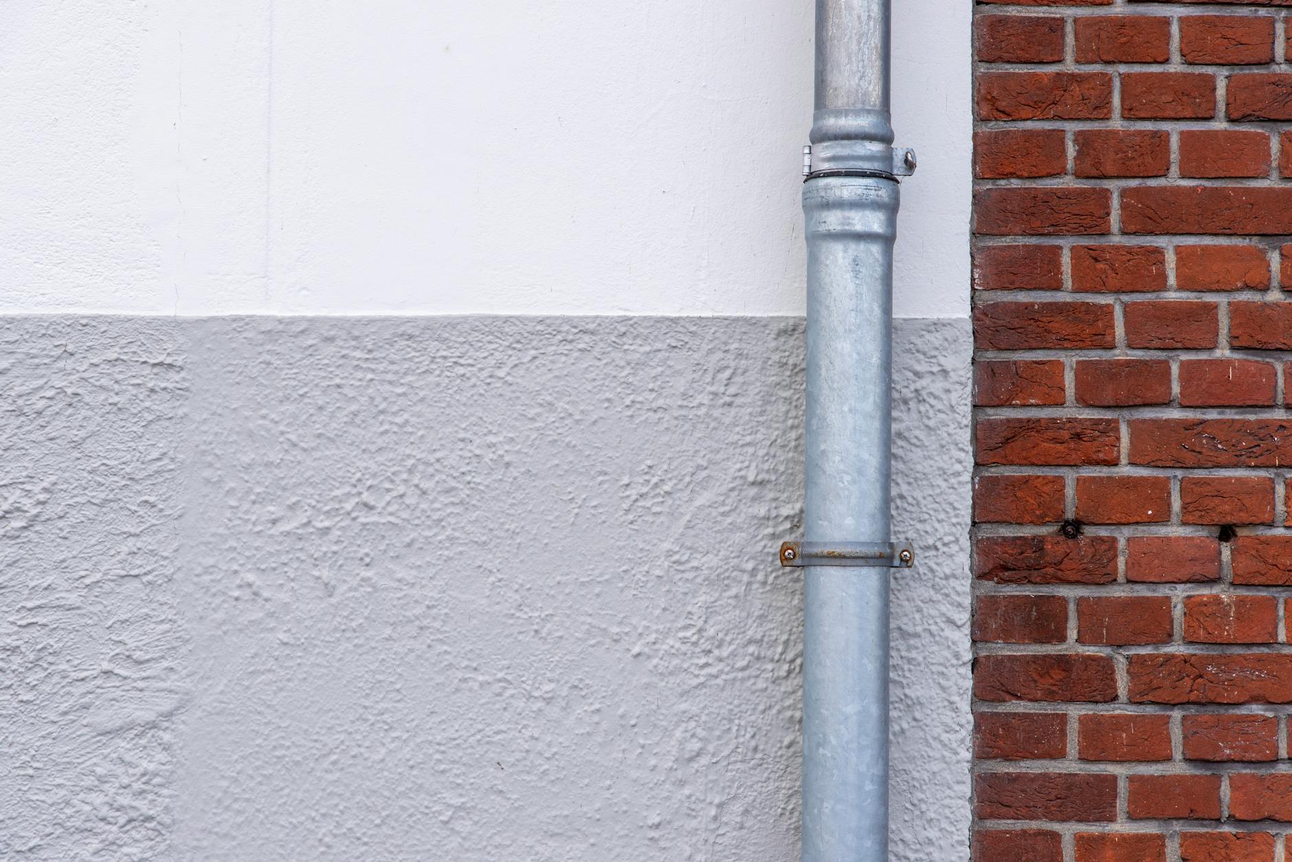 Close-up of a brick wall with a metal drainpipe against a textured white wall.