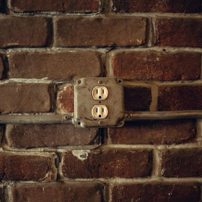 Rustic exposed brick wall featuring aged electrical sockets and metal conduit.