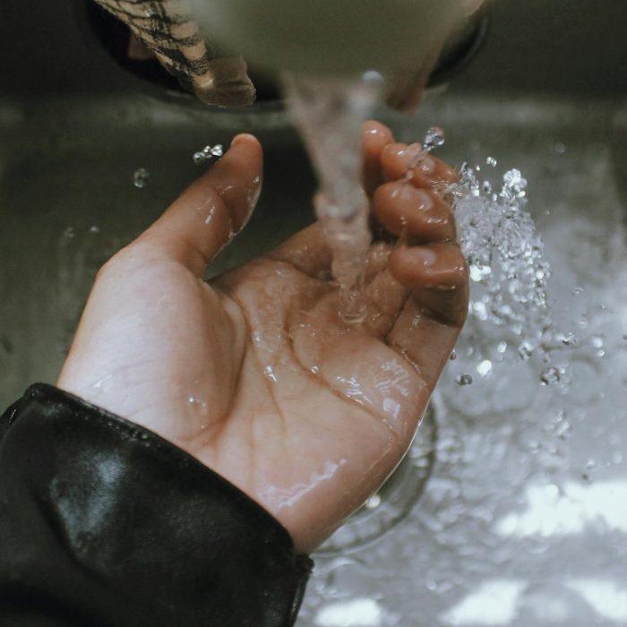 Close-up of a hand being washed under a stream of running water in a sink, emphasizing cleanliness.